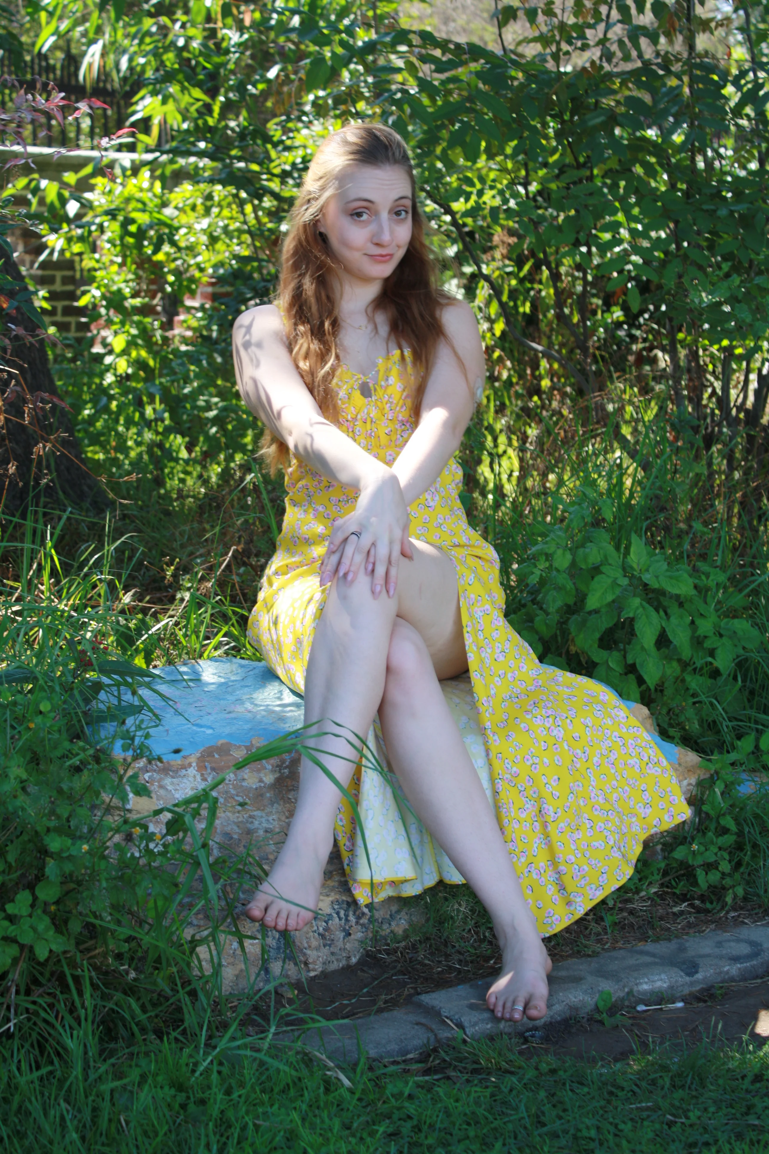 Jordie Morris sitting with crossed legs on a blue-painted rock at the Exposition Park Rose Garden.